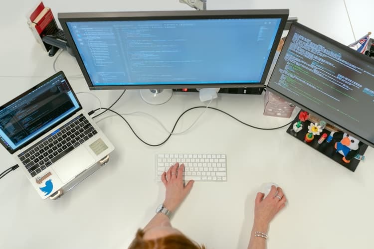 person coding with 3 screens