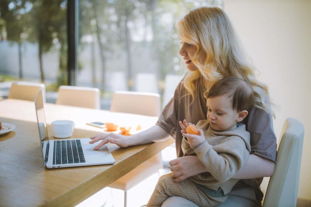 Woman working on a laptop with her kid at home. Coding Bootcamp for Women