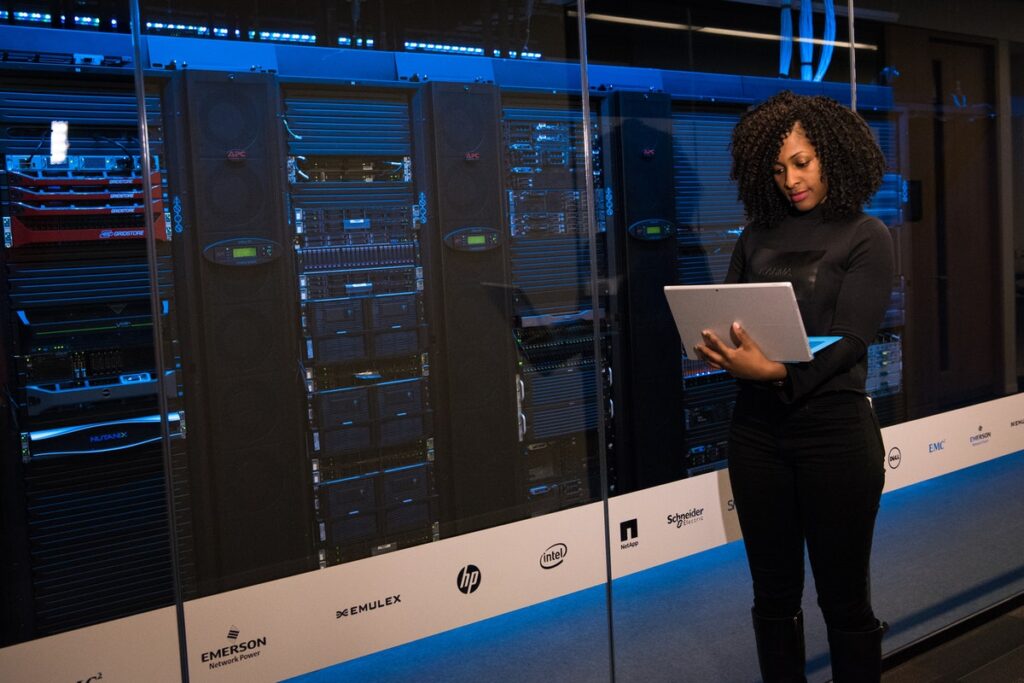A female engineer holding a laptop and typing in front of massive computer servers. LGBTQ+ Coding Bootcamp Scholarships