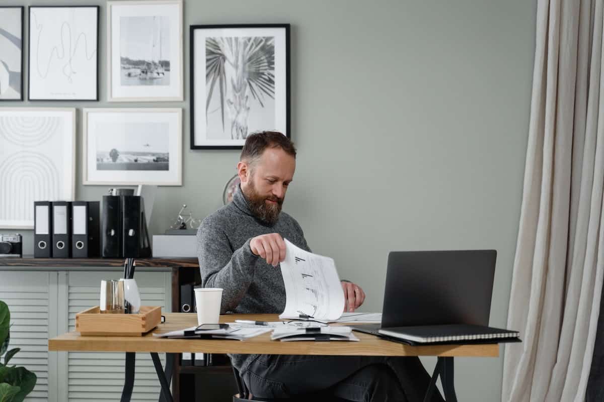 A man sitting at a desk with a laptop and going through a document.