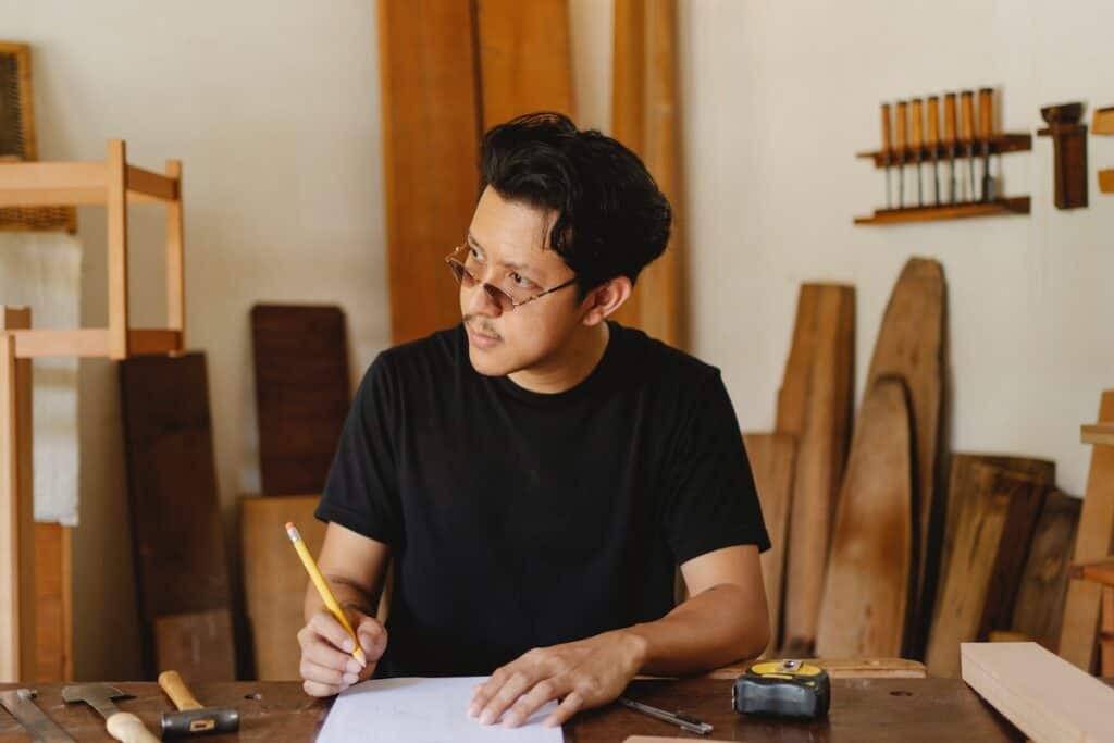 a thoughtful man designing a project with a pencil and paper in a carpentry workshop.