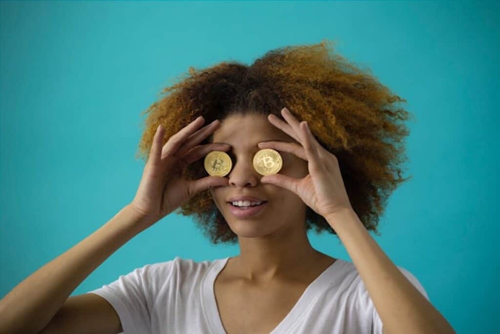 A woman holding up two pieces of Bitcoin and covering her eyes with them.