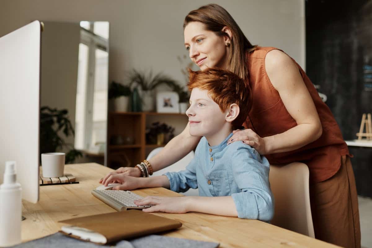 Male child learning at a desktop computer with a female adult supervising