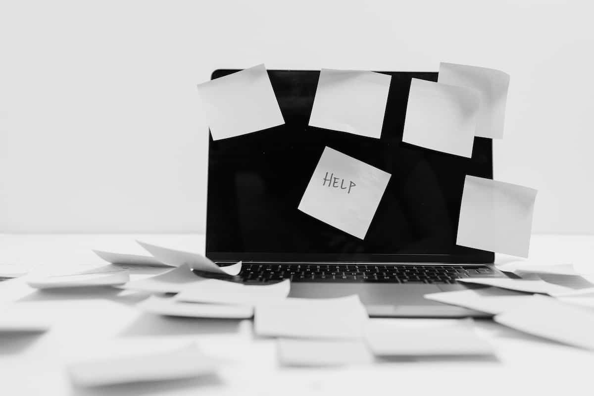 Laptop covered in and surrounded by sticky notes, one with “HELP” written on it