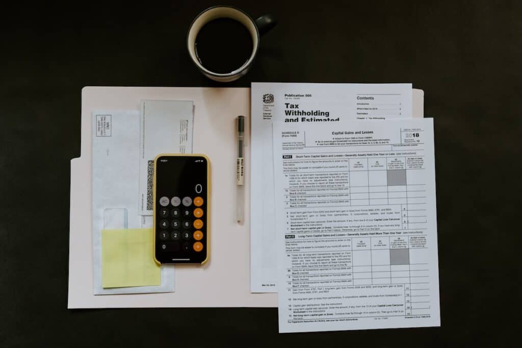 Accounting documents against a dark background with an iPhone and a pen on them and a cup of coffee on the side.