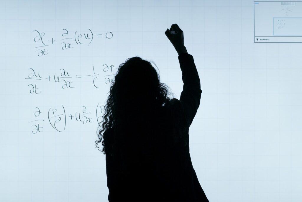 Silhouette of a woman working on a math assignment by writing a math equation on a whiteboard
