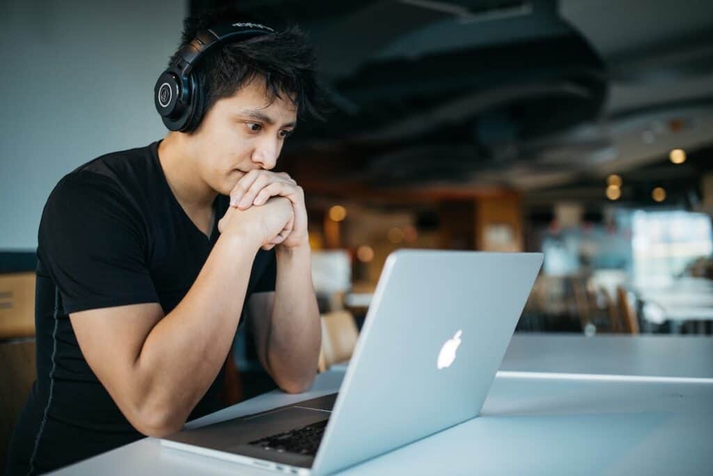 man wearing headphones in front of a laptop with wide eyes and clasped hands