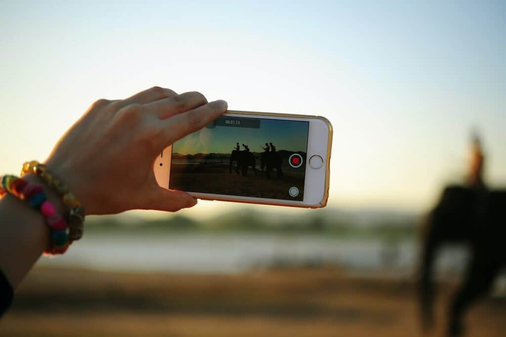 A person uses a smartphone to take a video of people riding elephants