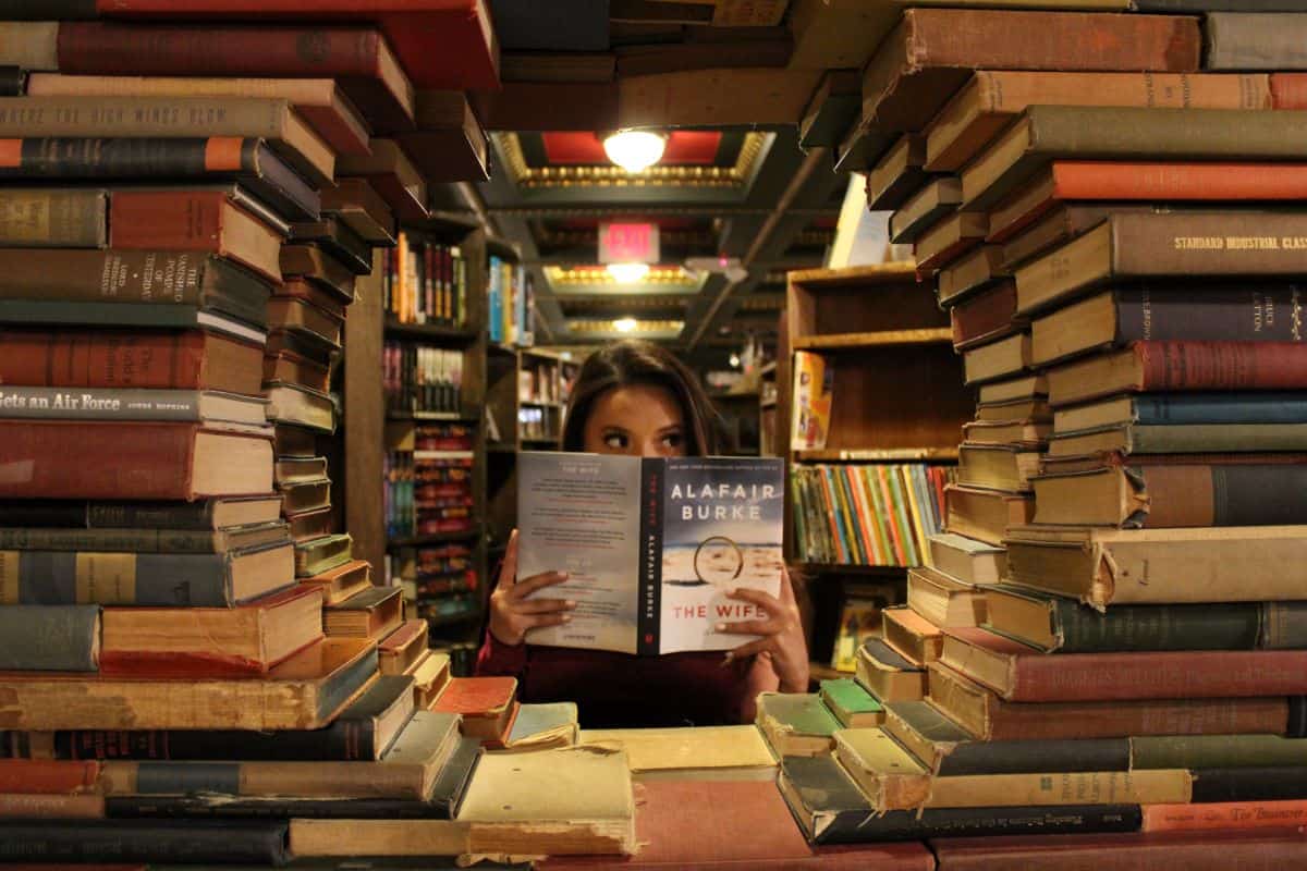 A lady standing in a section of a library with a book in hand
