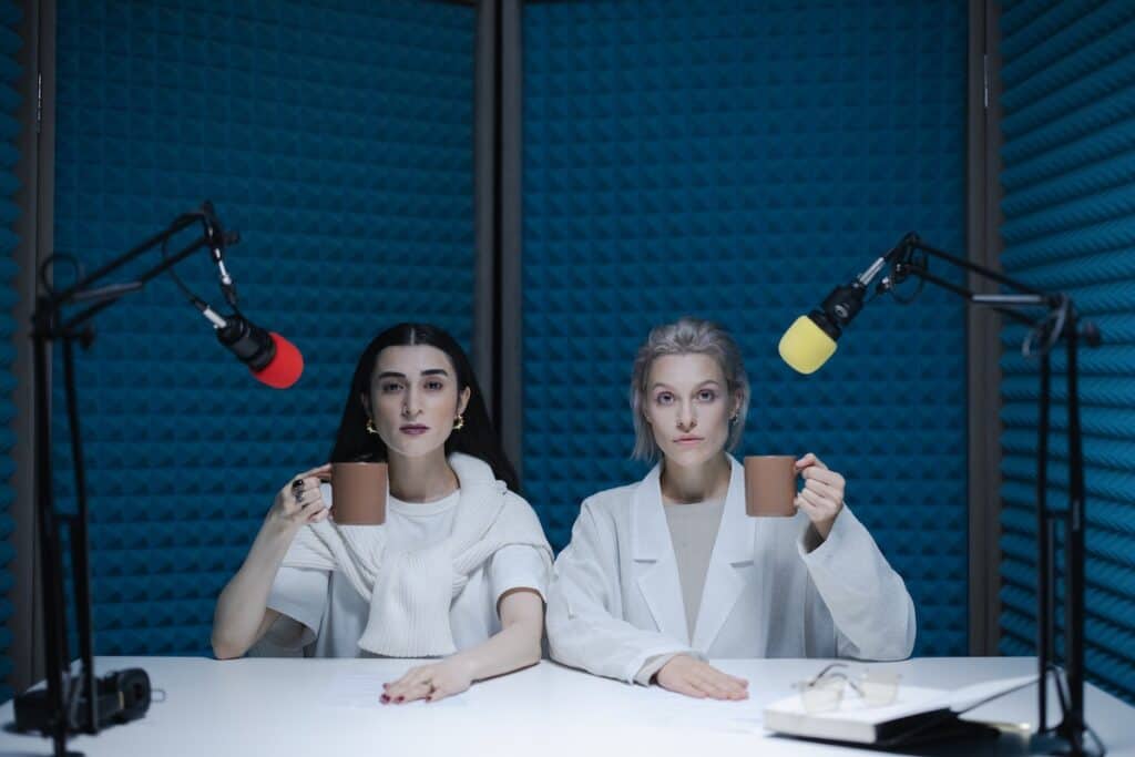 Alt-text: Two ladies dressed in white each holding a brown mug with microphones on their sides.